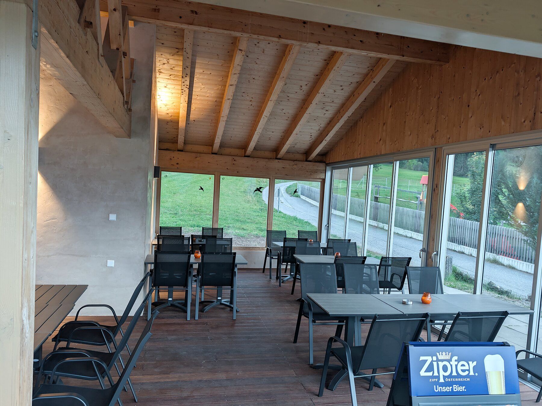 Überdachte Terrasse mit Holzdecke, Tischen und großen Fenstern